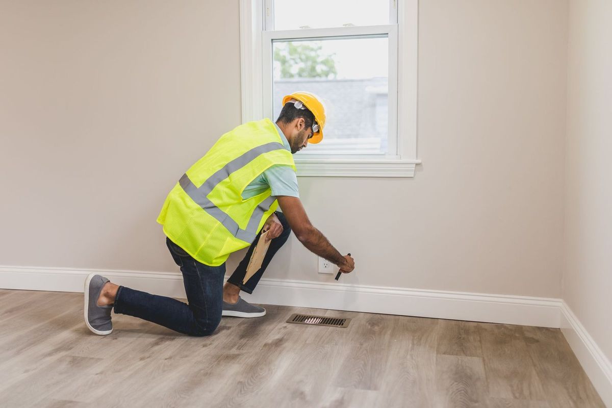 Technician in a high-visibility vest checking a baseboard