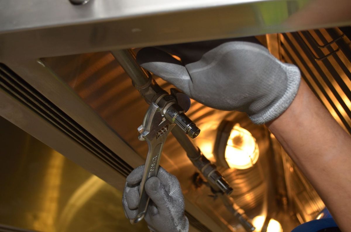 Gloved hands working on a water connection behind an appliance